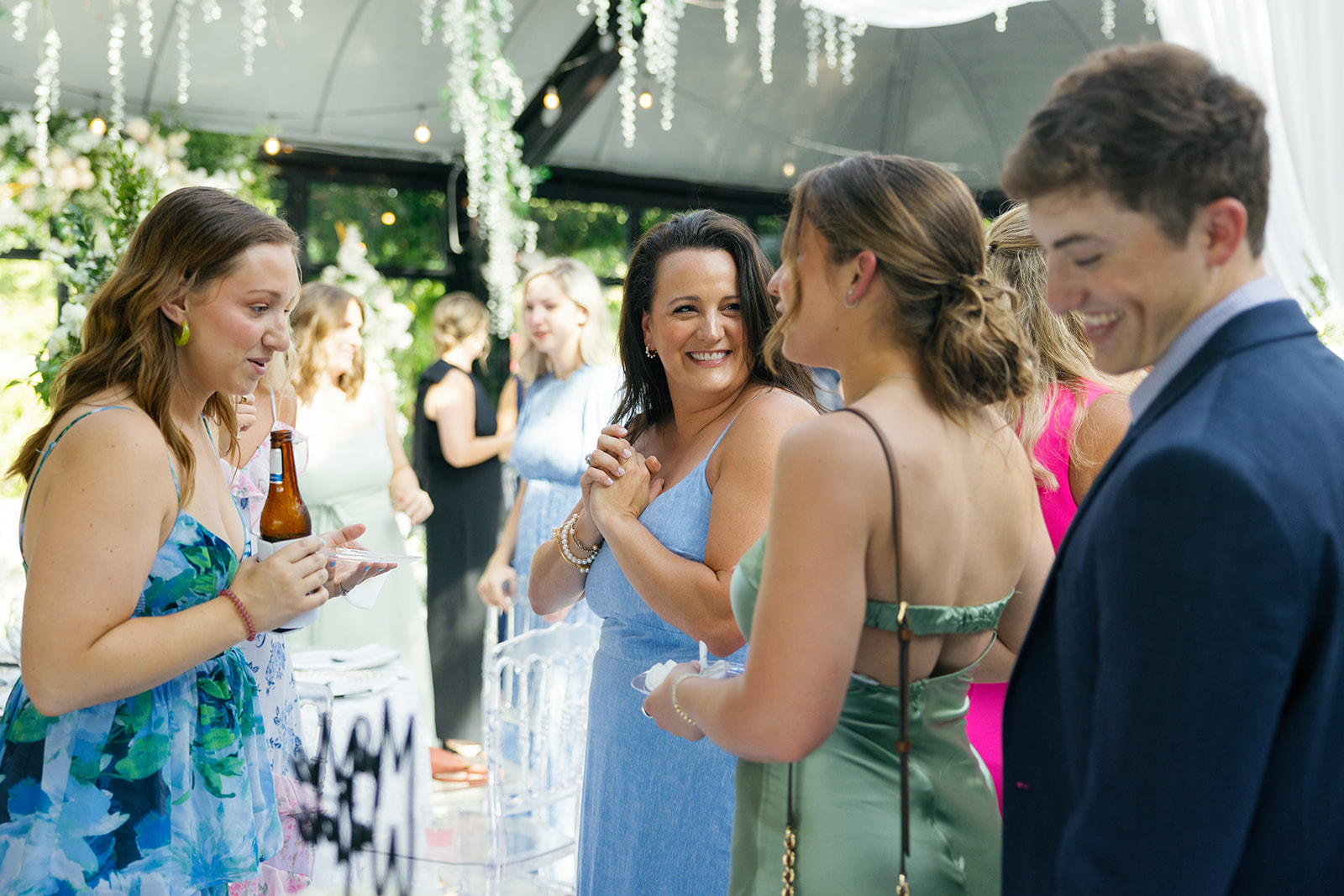 Women in colorful dresses and a man in a navy suit share a laugh while mingling at the reception.