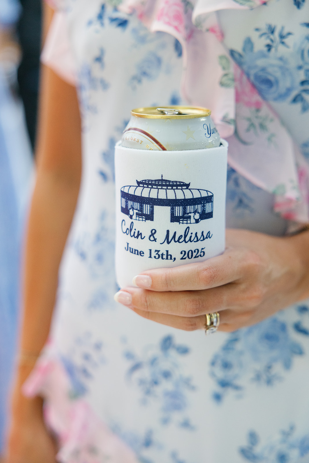 A close-up of a can in a koozie with the couple’s names, Colin & Melissa, and their wedding date, June 13th, 2025.