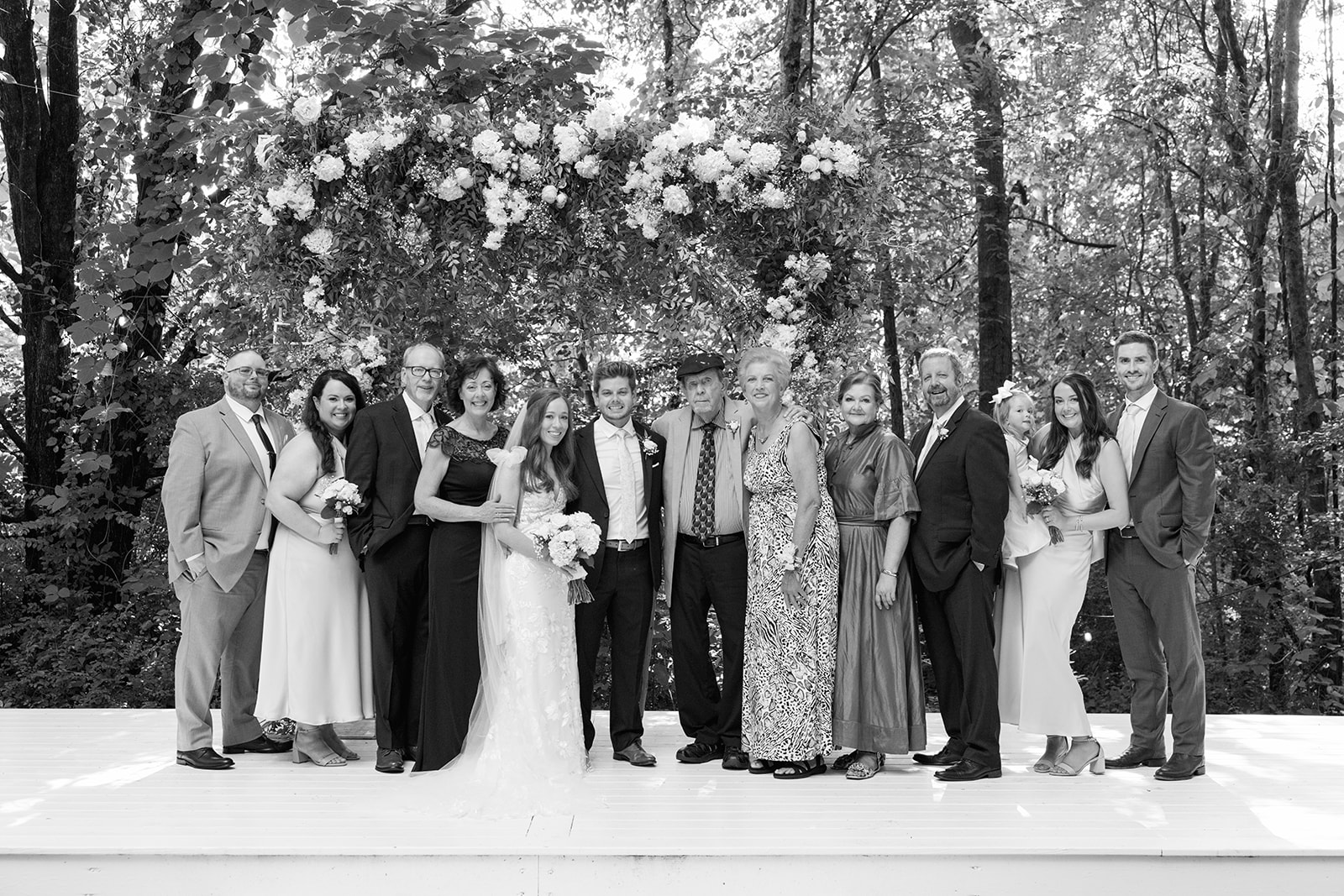 Large extended family group photo of bride and groom surrounded by relatives under the floral arch.