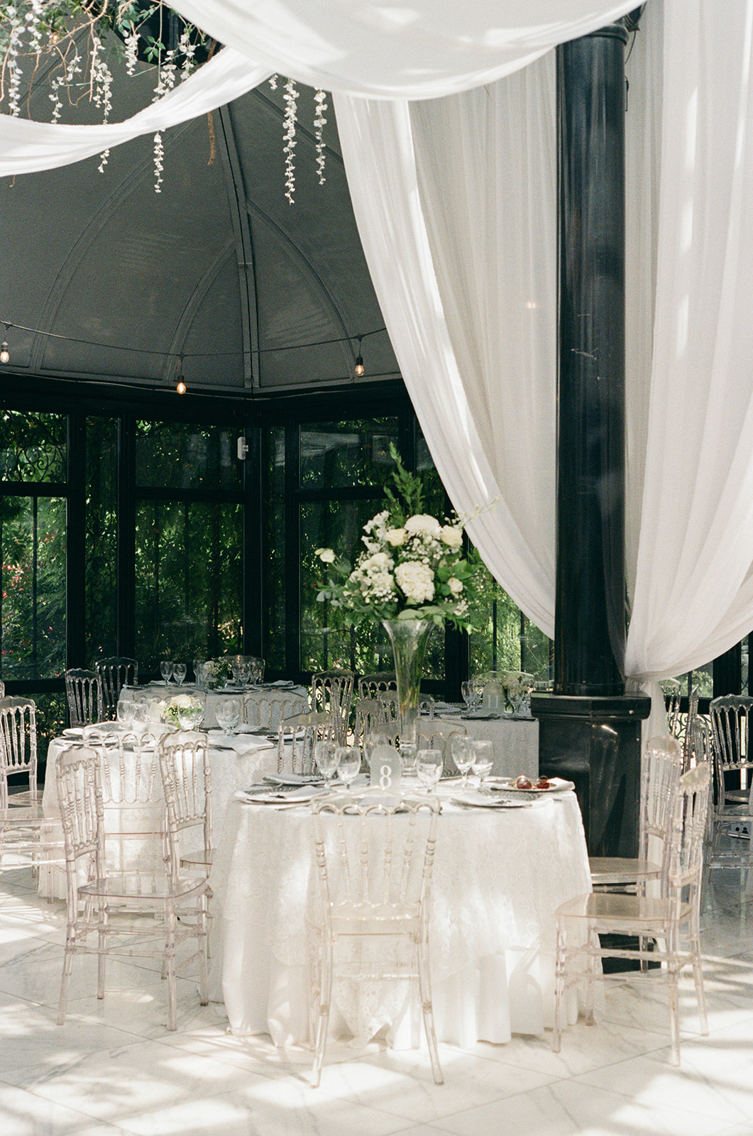 Elegant wedding reception setup at Edinburgh West in Greenville, SC, with round tables, clear chairs, and tall floral centerpieces, photographed in soft natural light.