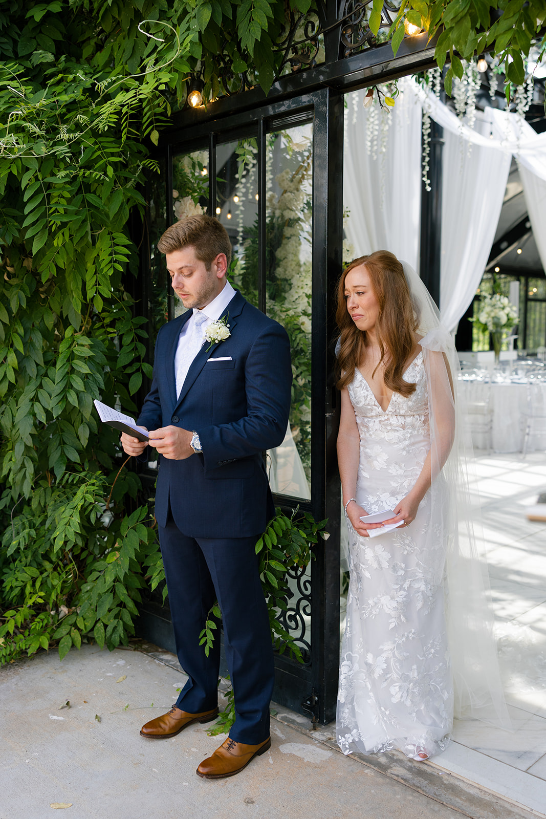 Groom reads vows aloud as the bride listens, leaning against the doorway during their first touch at Edinburgh West – a timeless candid wedding photo in Greenville, SC.