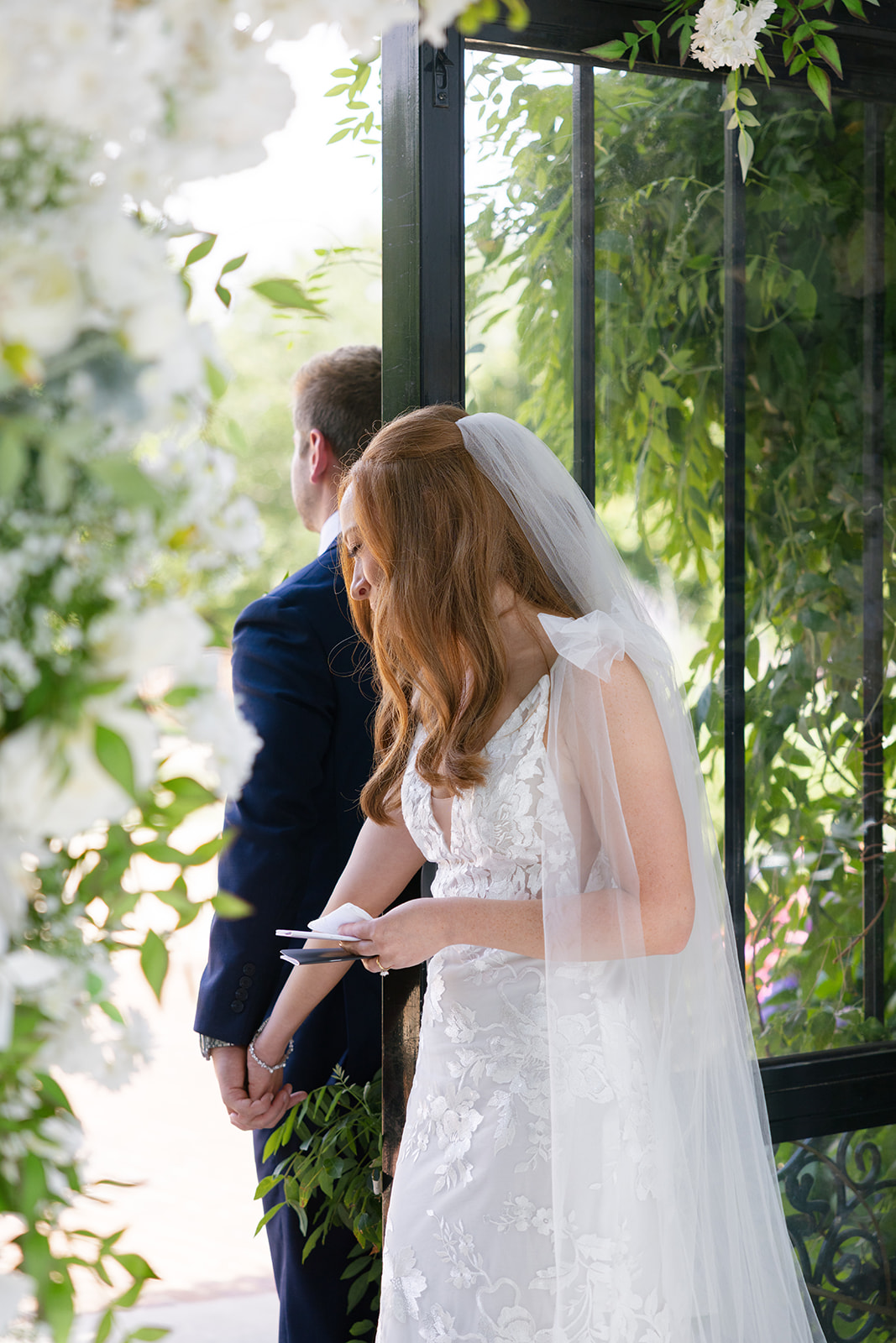 Bride and groom stand back-to-back holding hands around a doorway at Edinburgh West, reading private wedding vows in an emotional candid moment – captured by a Greenville wedding photographer.
