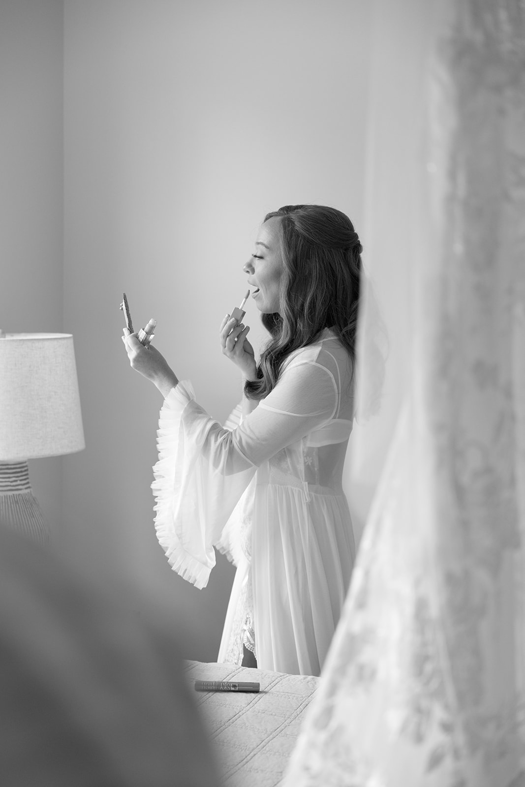 Black and white photo of the bride applying lipstick in her bridal robe during candid wedding photography in Greenville