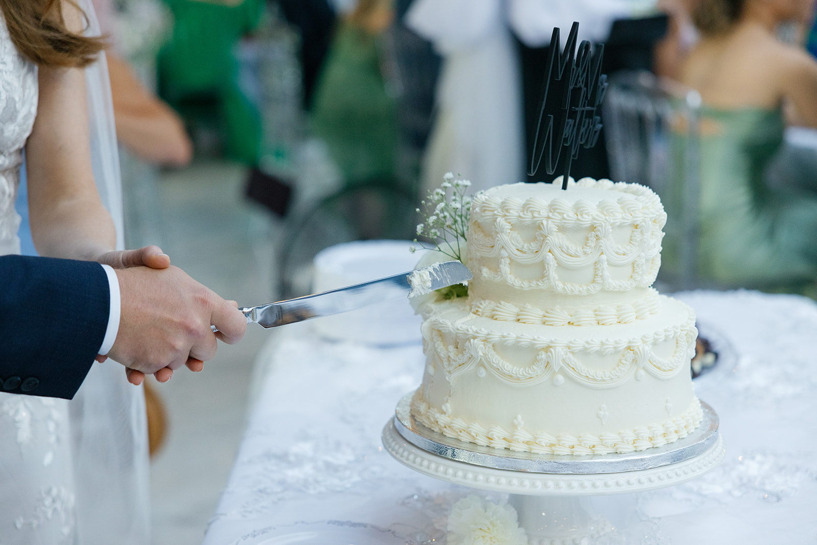 Close-up of the groom using a cake server to place a slice of the white wedding cake onto a plate.