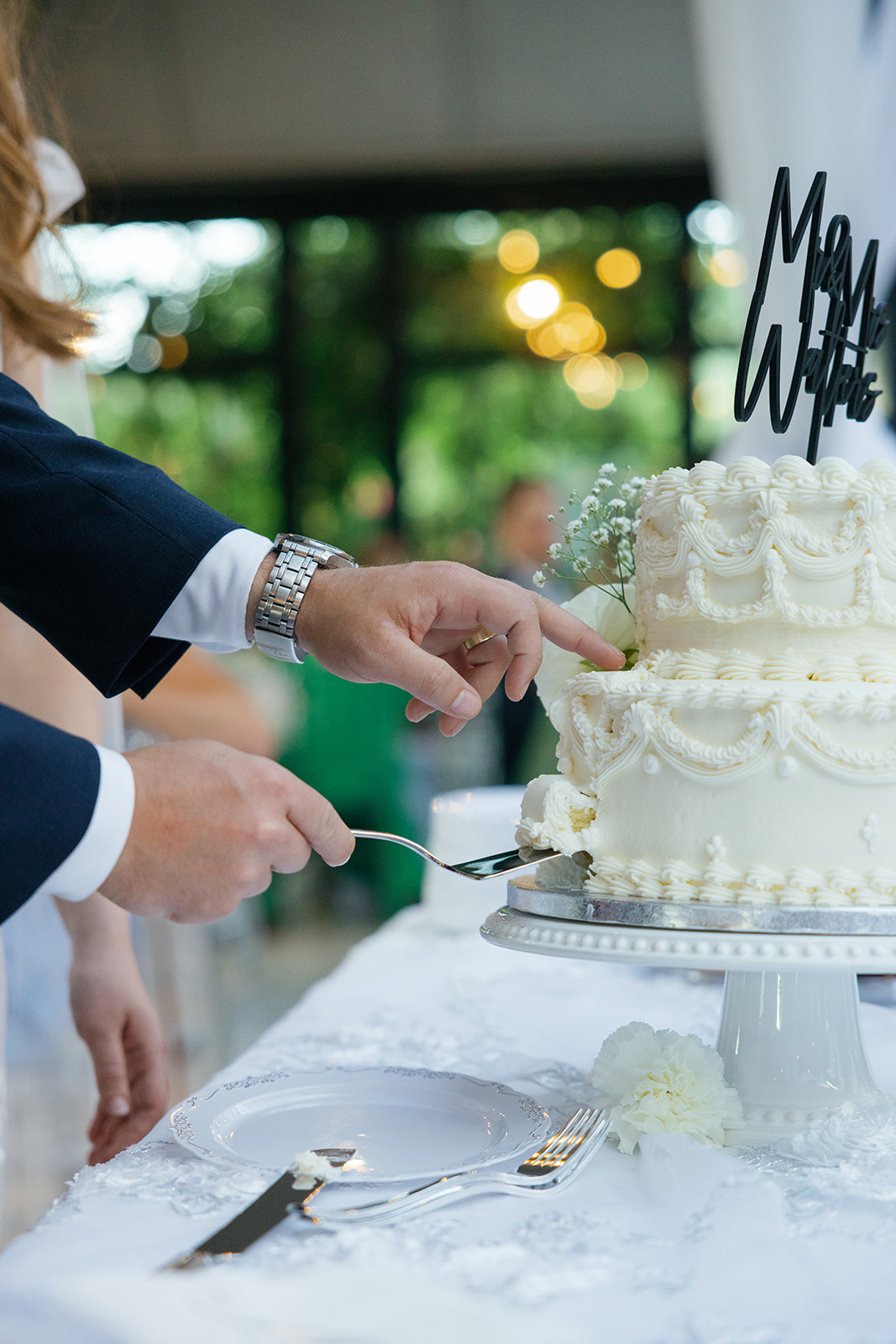 Close-up of the bride and groom cutting into their white tiered wedding cake decorated with piped icing.