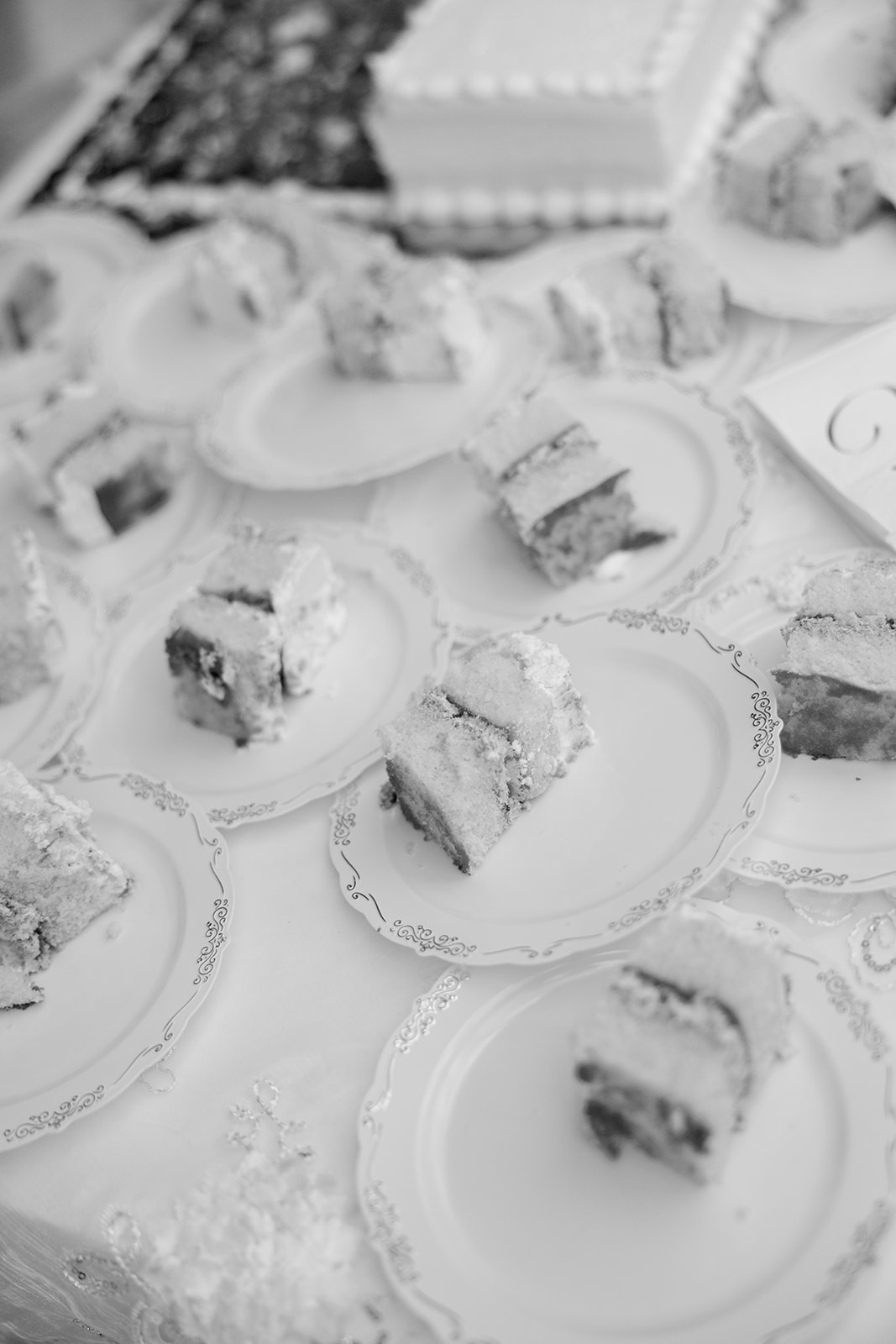A black and white photo showing multiple plates topped with slices of wedding cake on a decorated table.