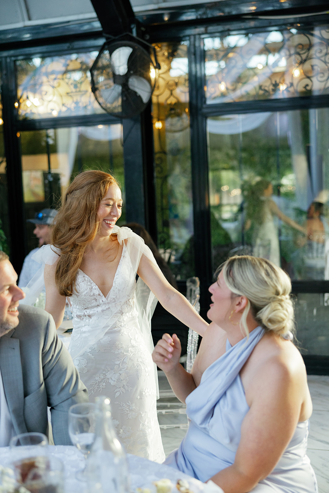 The bride smiles warmly while chatting with seated guests during the reception.