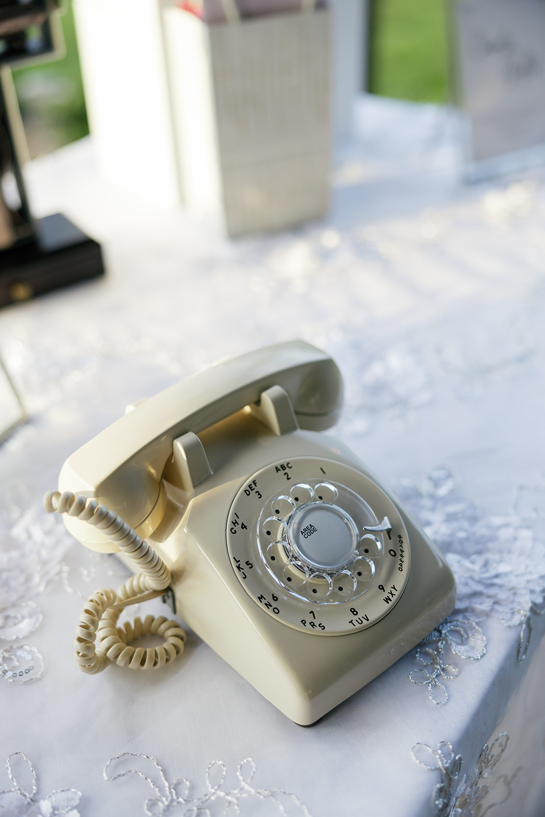 A vintage cream rotary phone sits on a lace-covered table as part of the wedding décor.