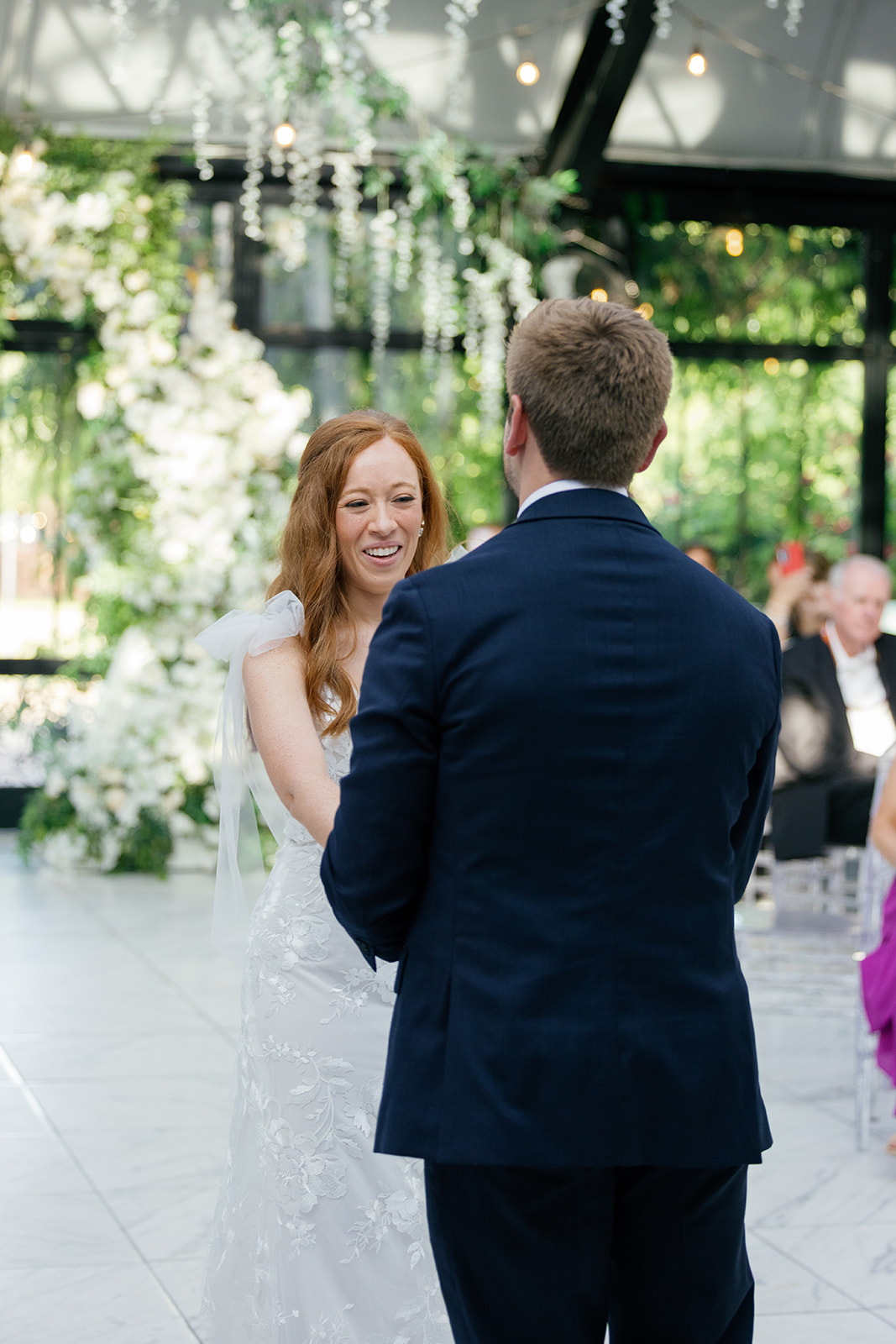 Bride smiles at the groom while holding his hands during their first dance.