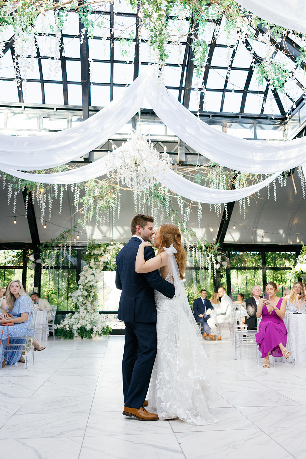 Bride and groom share their first dance under draped fabric and chandeliers.