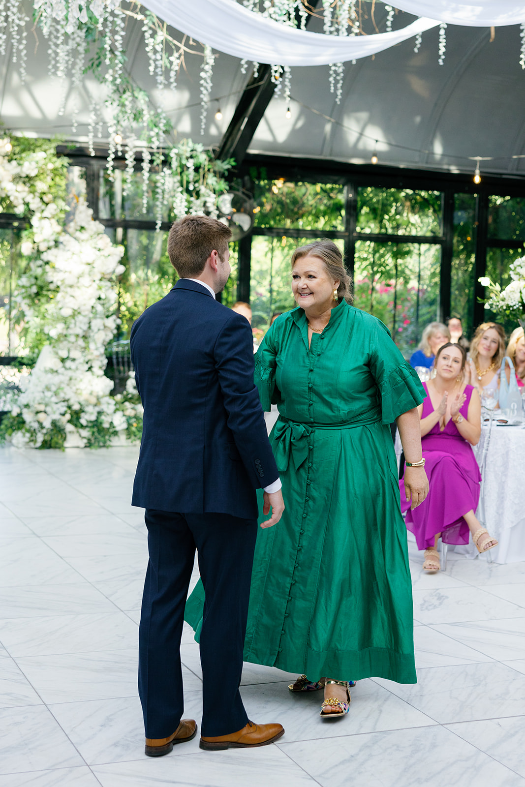 Groom shares a joyful dance with his mother, who wears a vibrant green dress.