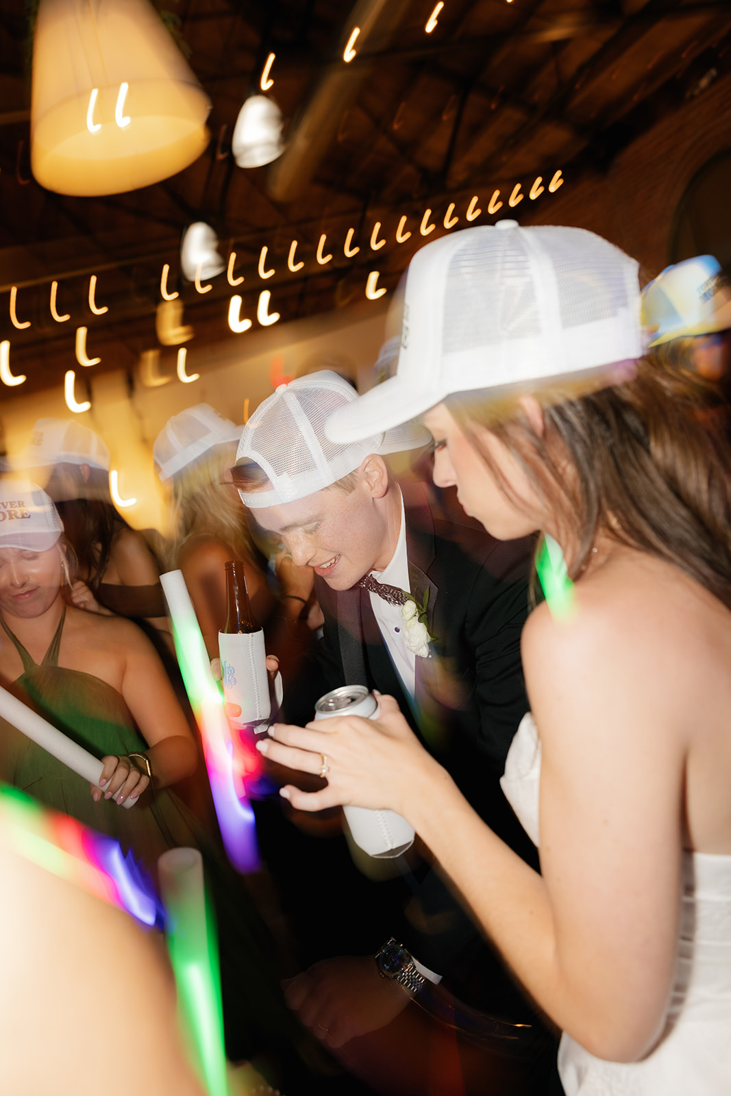 Bride and groom wearing white hats and dancing closely with glowing lights streaking through the image.