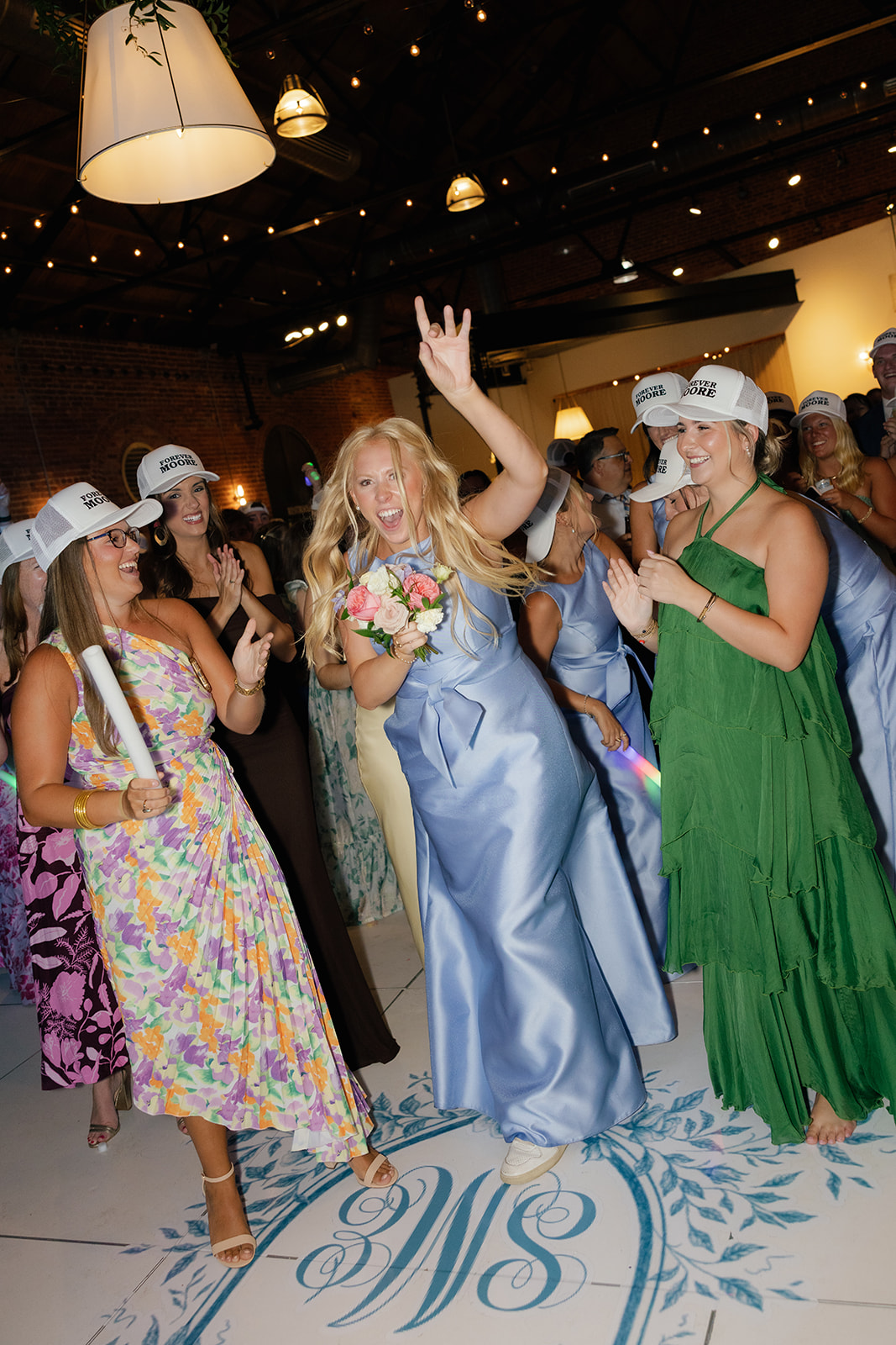 A bridesmaid in a blue satin dress celebrates catching the bouquet on the custom monogrammed dance floor.