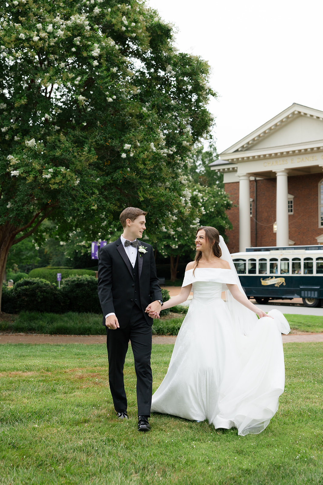 Bride and groom on a grassy lawn with trees and a trolley in the background – wedding planning advice: schedule relaxed outdoor portraits for natural, joyful moments.