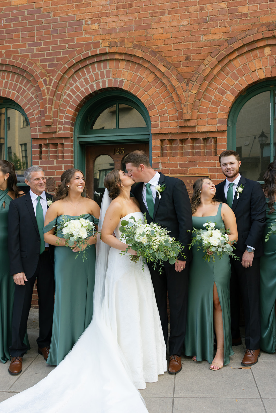 the bride and groom kissing with their wedding party besides them