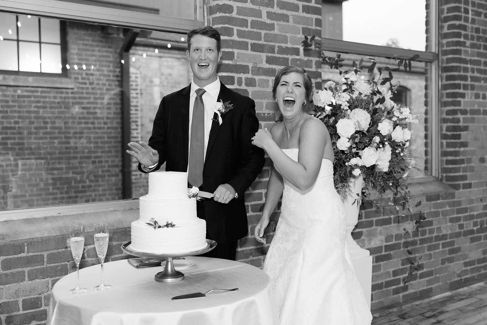 the bride and groom laughing as they cut their cake 